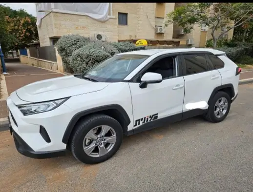 מוניות בפריסה ארצית - חזית וצד של מונית טויוטה RAV4 לבנה (SUV) חונה ברחוב.